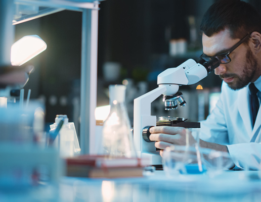 A scientist in a lab coat looking into a microscope.